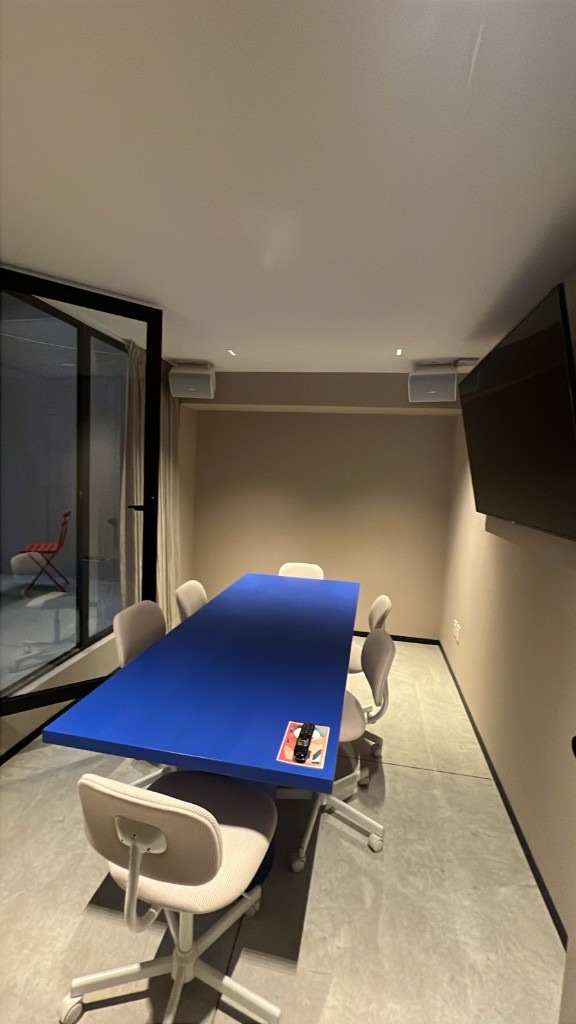 Oficina privada con mesa azul para hasta 10 personas, pantalla y ventanal al patio
