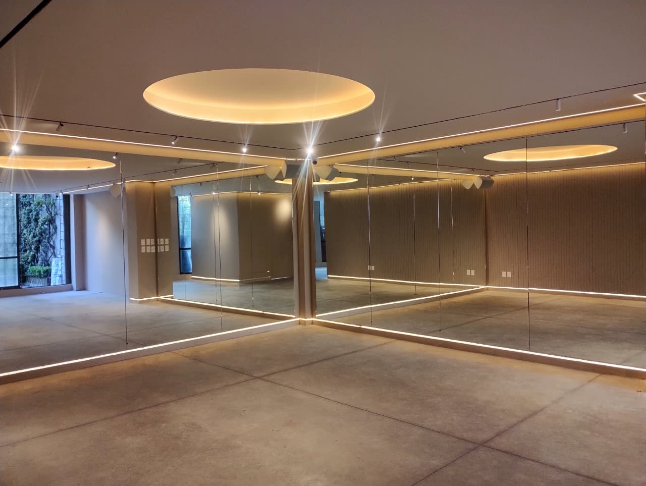 Salón del Estudio Popnest en Coyoacán: espejos de piso a techo, iluminación cálida y concreto pulido